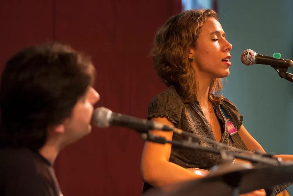 Mariane Guerra cantando ao microfone com violão em show ao vivo